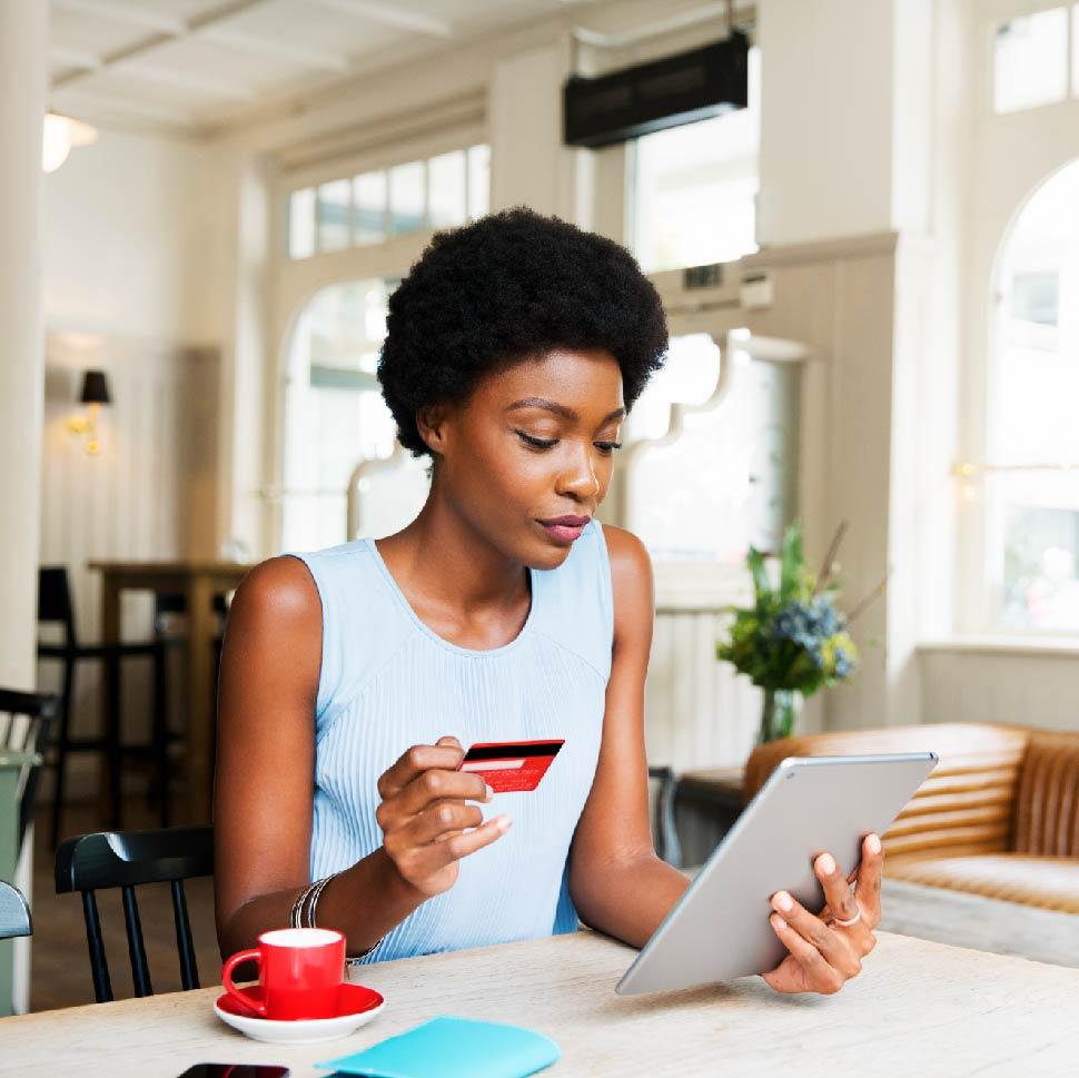 woman holding a tablet and credit card, making a purchase with a red coffee cup beside her