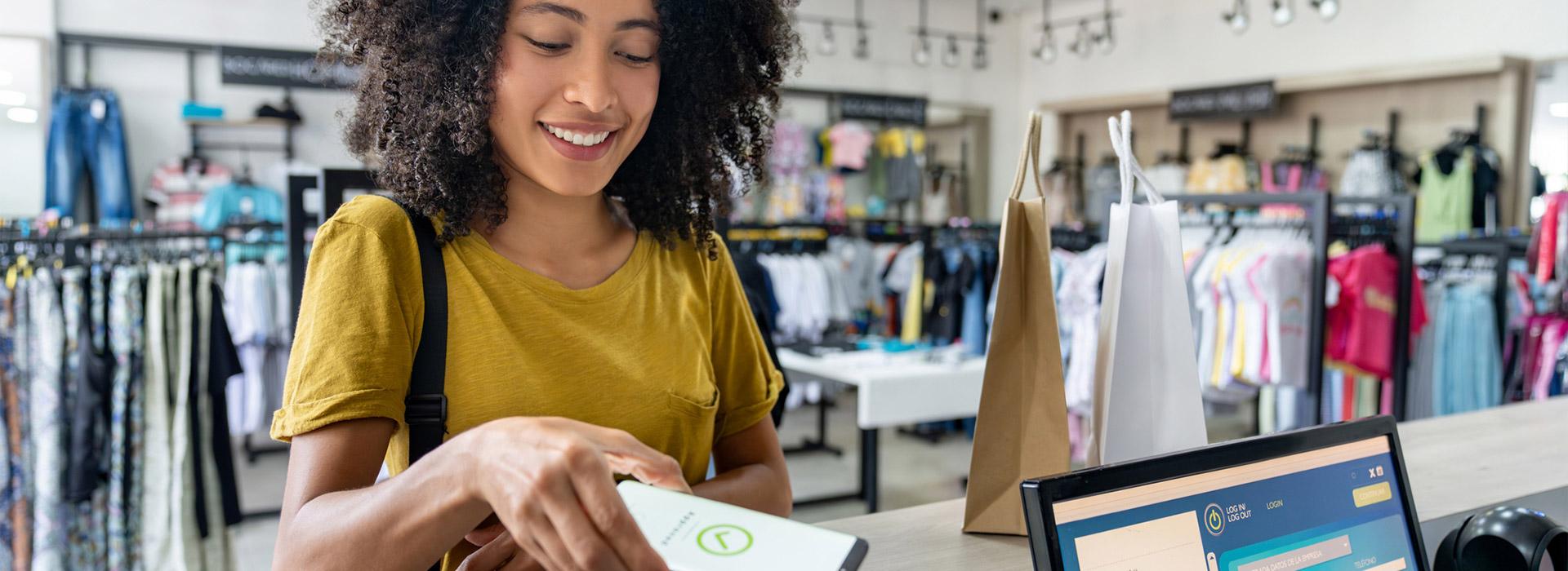 Young woman making purchase in clothing store using mobile wallet