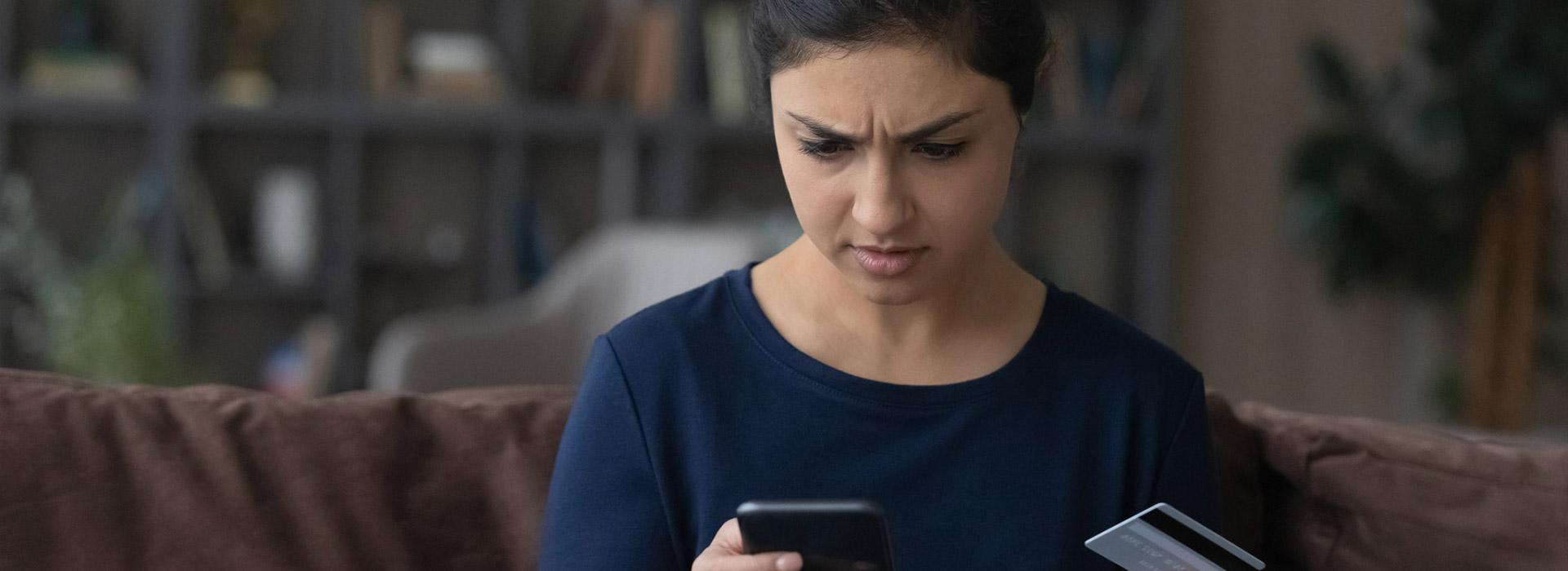 confused lady looking at her cell phone and credit card