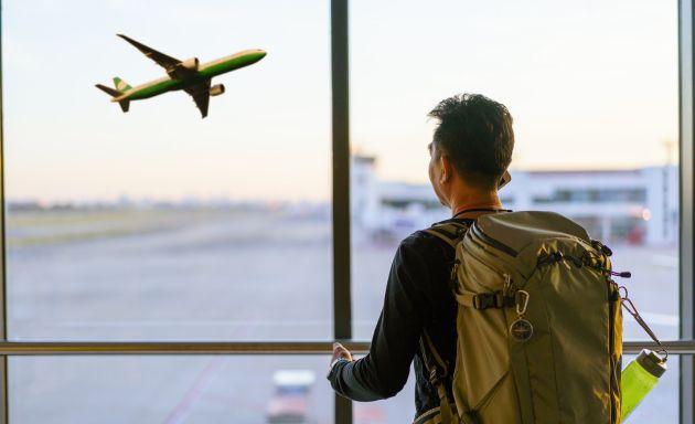 Man looking out of airport window at an airplane