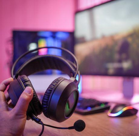 hand holding gaming headphones with computer in background