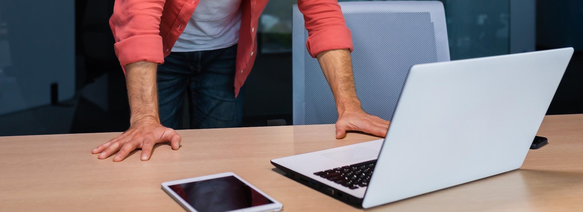 Man standing and looking down at computer and tablet
